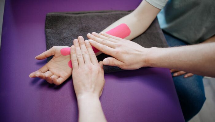 Close-up of hands applying pink kinesiology tape during a relaxing arm massage. - Photo by Danik Prihodko on Pexels