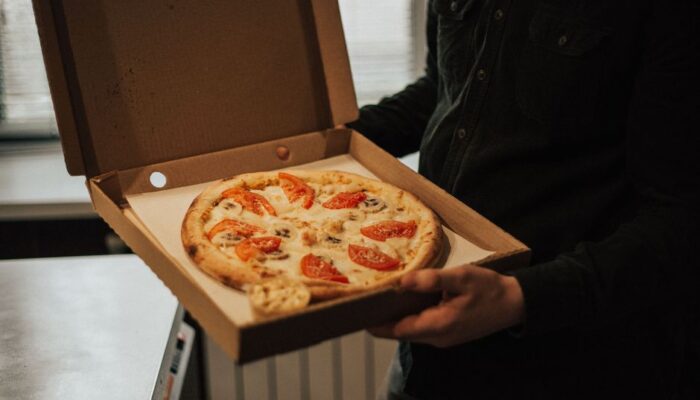 A person holds an open box with a freshly baked pizza topped with tomatoes and cheese. - Photo by Max Avans on Pexels