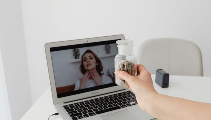 Person holding supplements during a virtual consultation with a doctor on a laptop. - Photo by www.kaboompics.com on Pexels