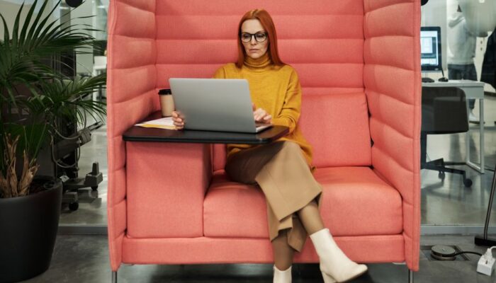 Businesswoman in a yellow sweater working on a laptop in a modern office booth setting, exhibiting style and focus. - Photo by Jack Sparrow on Pexels