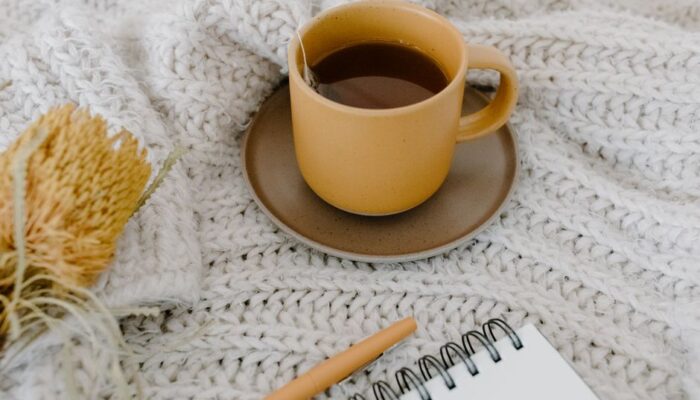 Warm tea cup with notebook and pen on a knitted blanket, creating a cozy ambiance. - Photo by Tara Winstead on Pexels