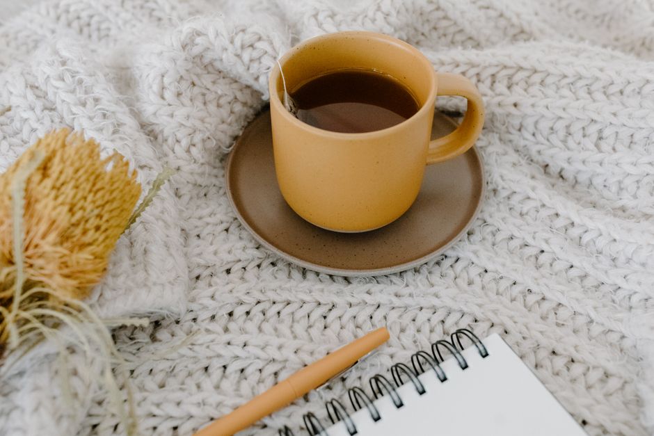 Warm tea cup with notebook and pen on a knitted blanket, creating a cozy ambiance. - Photo by Tara Winstead on Pexels